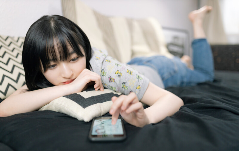 スマホアプリに熱中する休日を過ごす女子大生